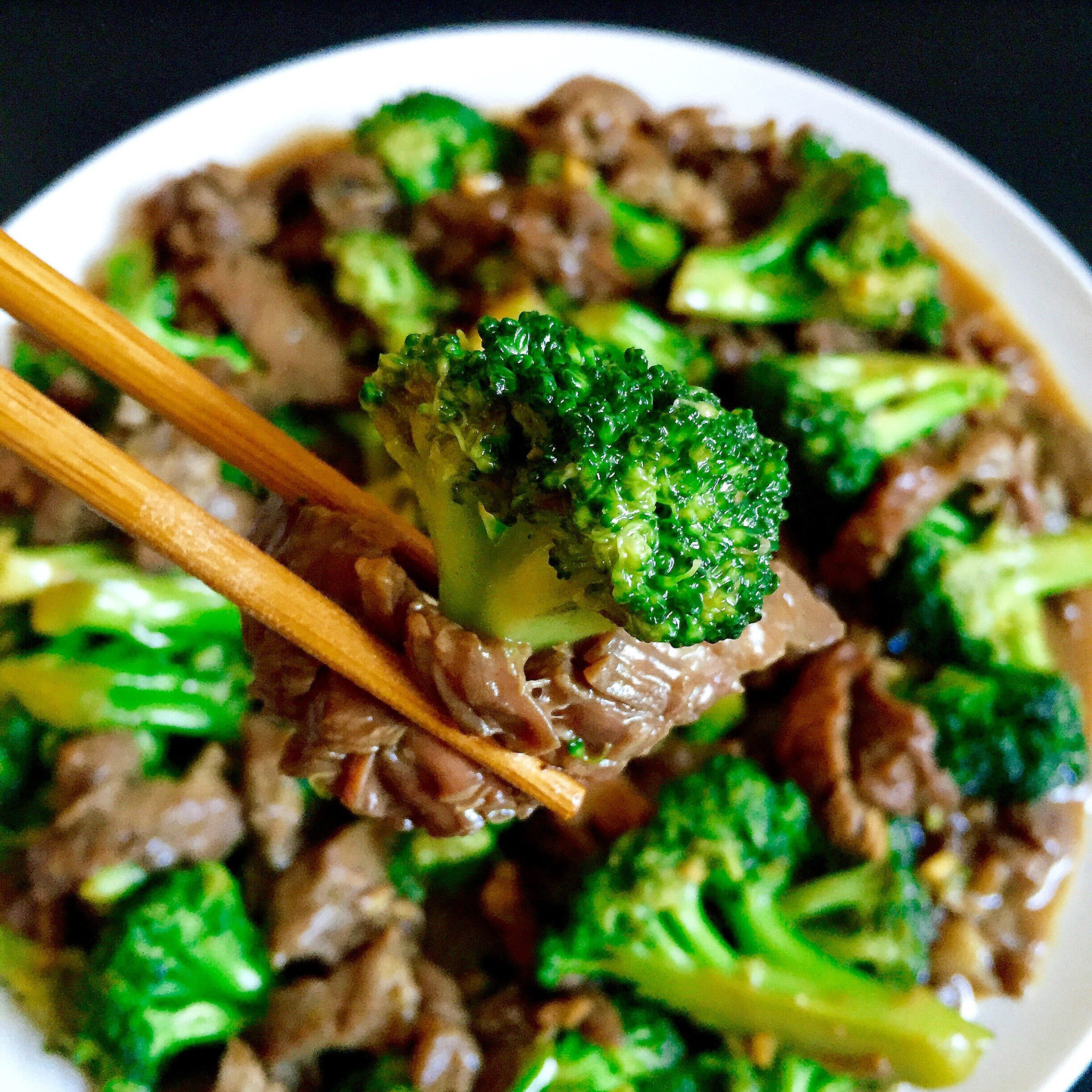 Chopsticks lifting a piece of broccoli from a plate of beef and broccoli