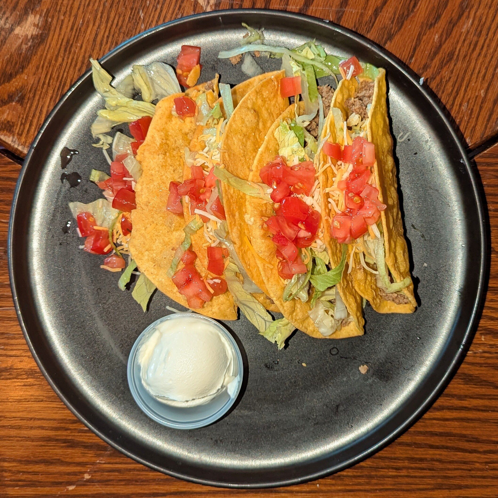 Three crunchy ground beef tacos with lettuce and tomato and a side of sour cream