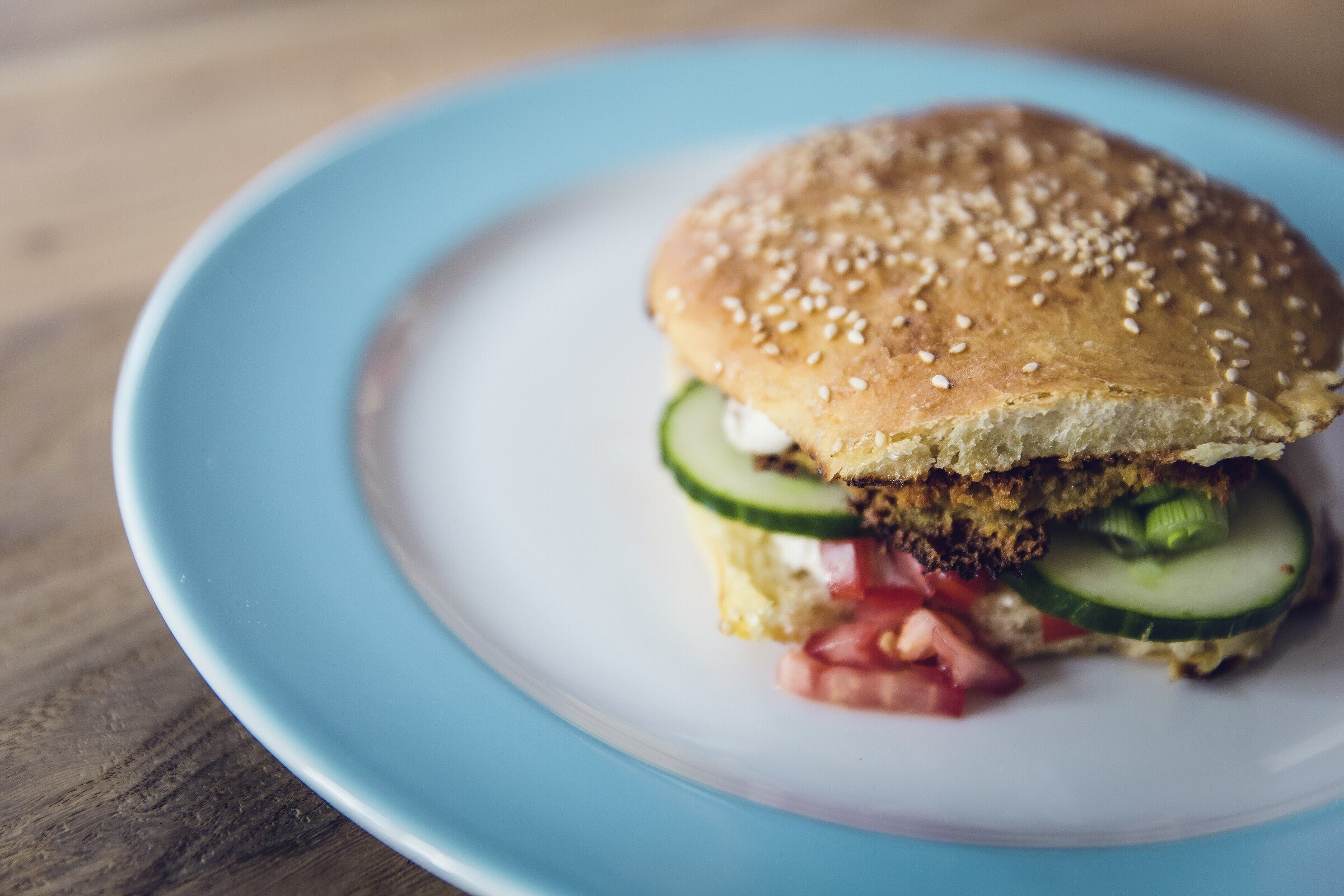 A black bean burger in a sesame bun with cucumber and red onion on a blue plate