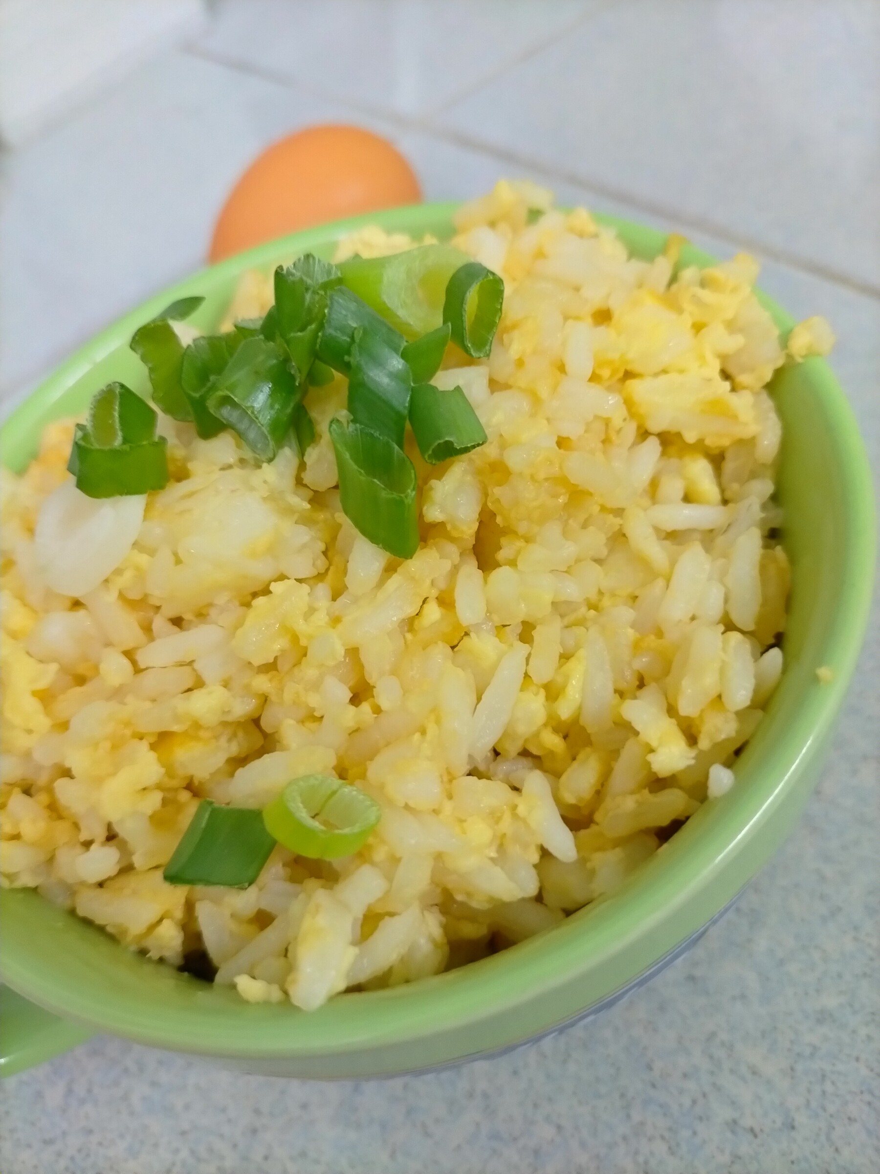 Egg fried rice topped with sliced green onions in a green bowl