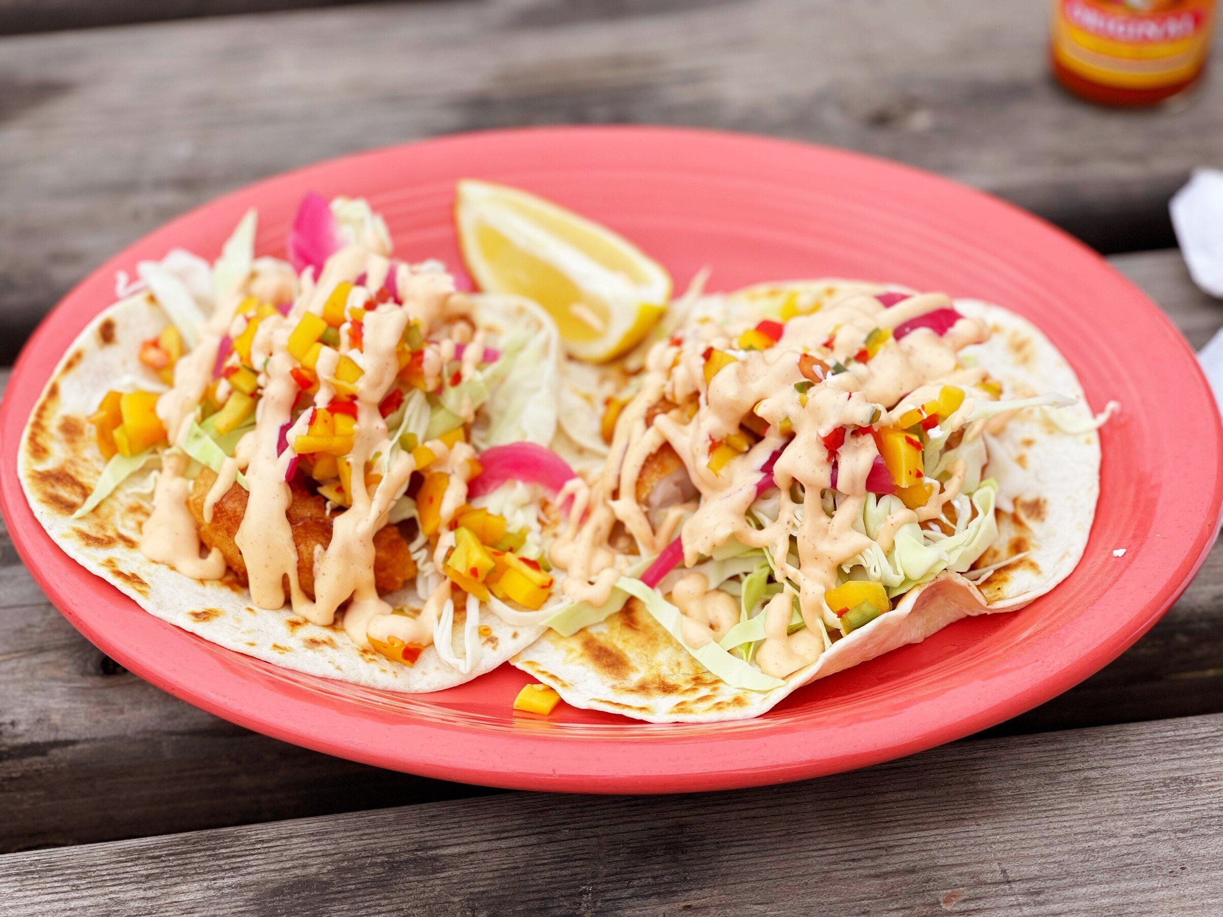Two shrimp tacos with cabbage slaw, creamy sauce and a lime wedge on a coral plate