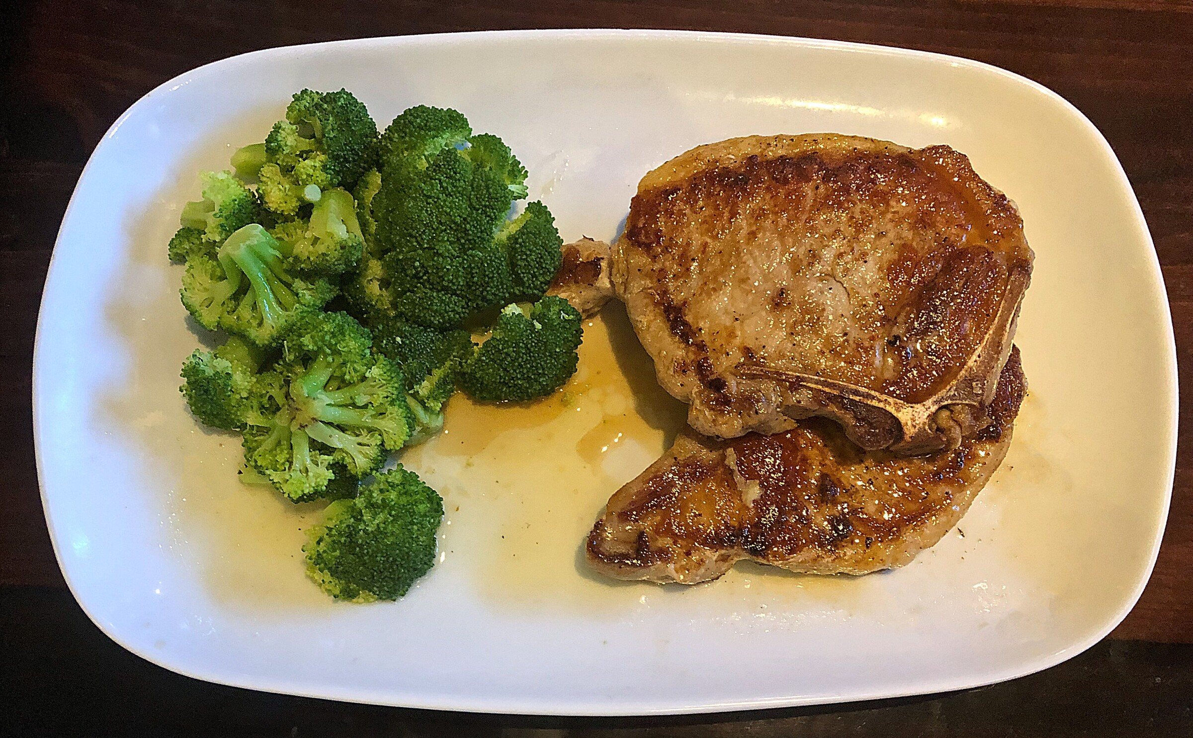 A pan-seared pork chop with broccoli on a white plate