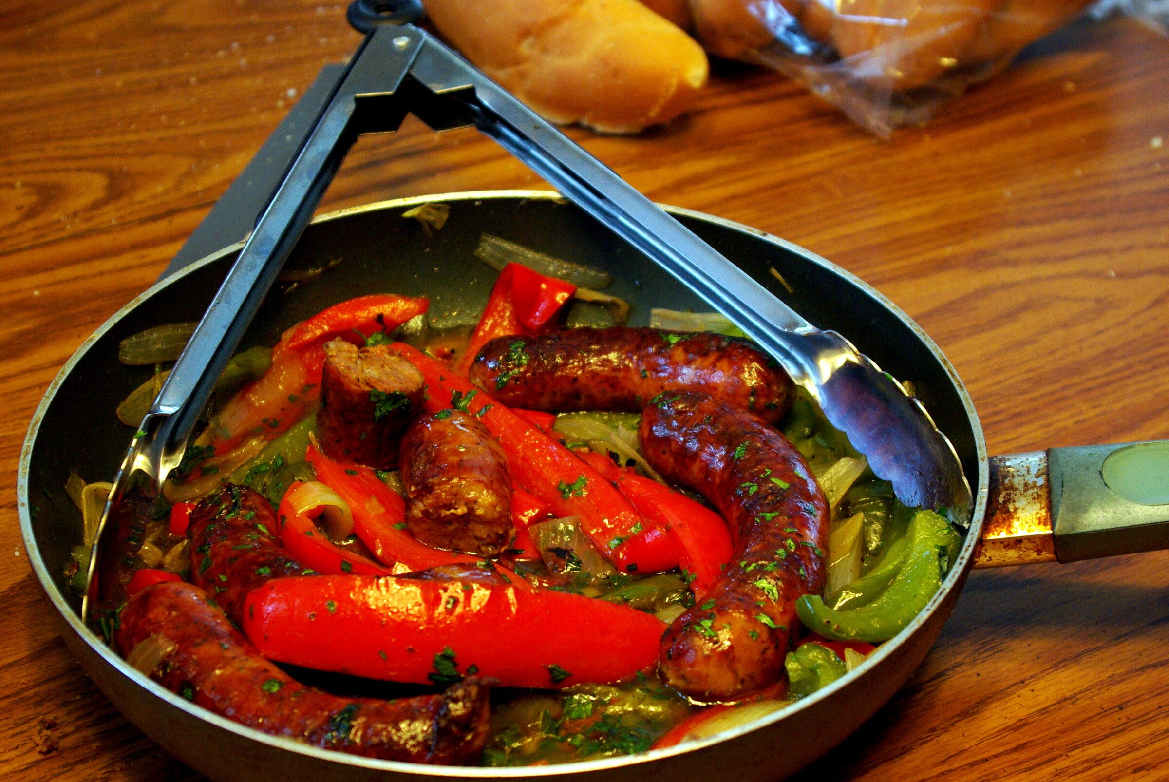 Italian sausages with red and green peppers in a skillet with tongs