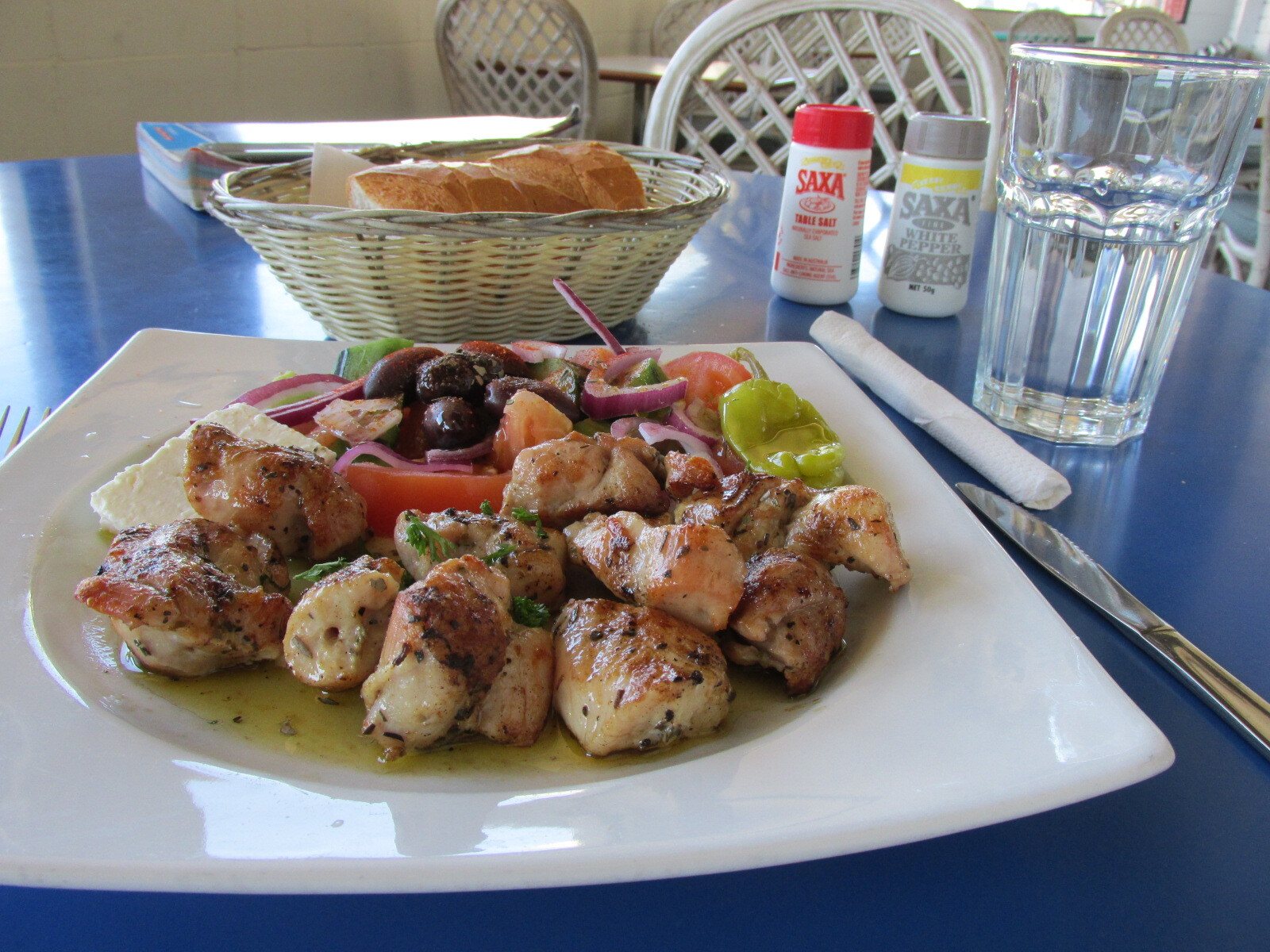 Pieces of grilled chicken souvlaki on a white plate with salad