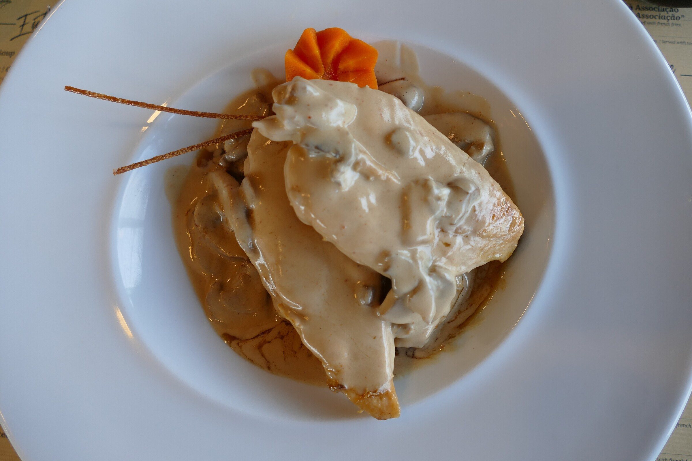 A chicken breast in a creamy sauce on a white plate
